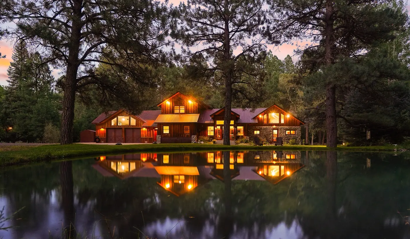 A warmly-lit timber home reflected in a still pond at dusk
